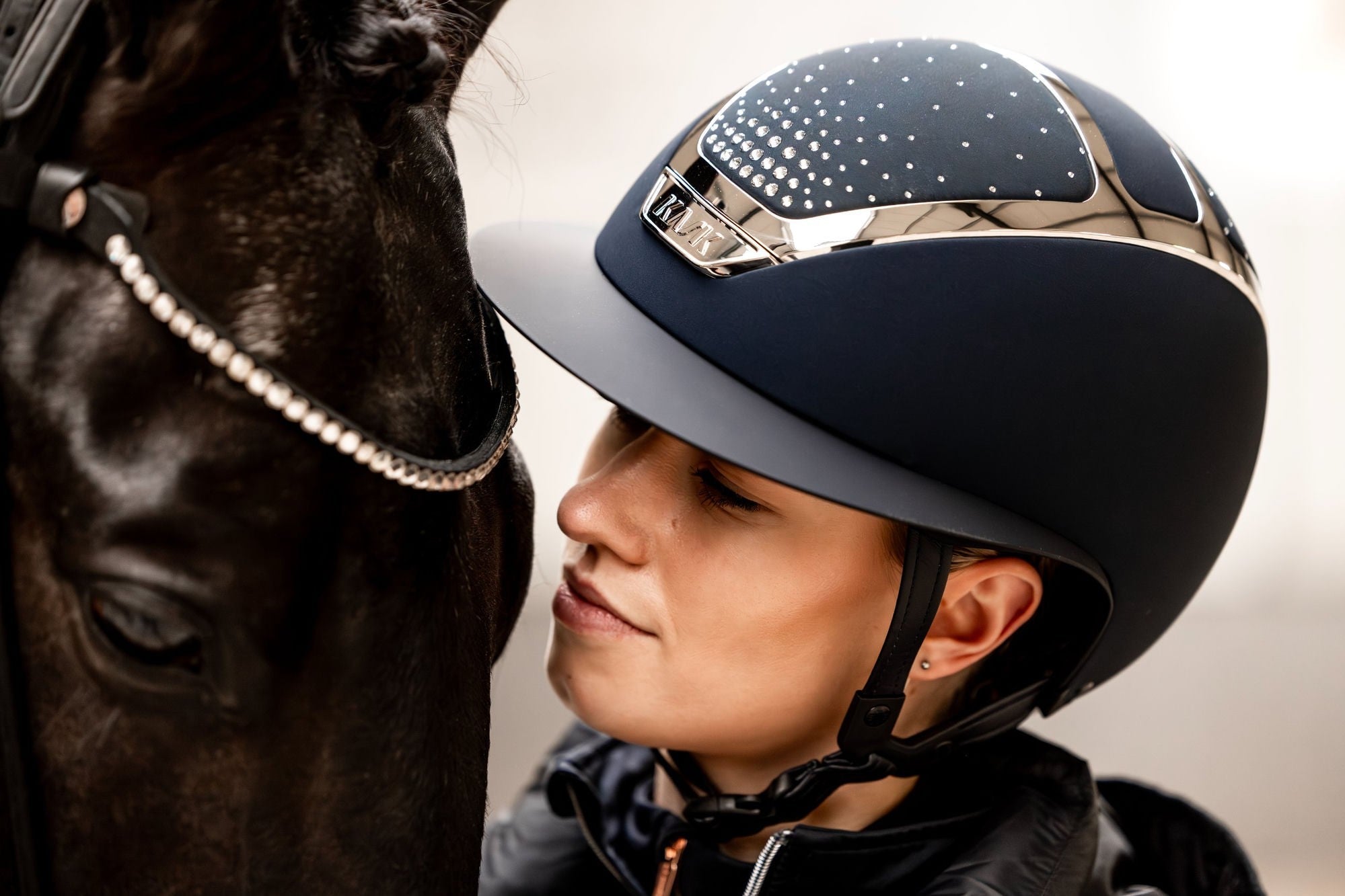 Reiterin mit KASK Reithelm Nase an Nase mit einem schwarzen Pferd